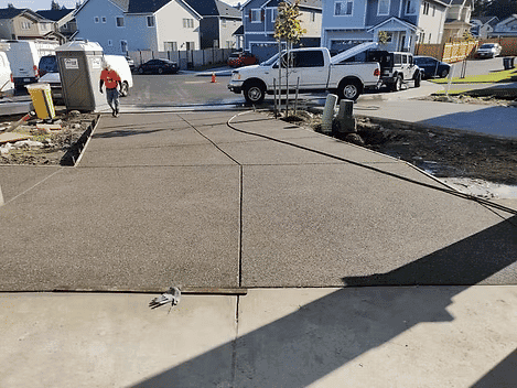 Newly poured concrete driveway with construction vehicles and residential homes in the background.