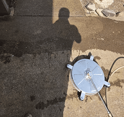 Concrete surface with pressure washer attachment and shadow of a person overhead.
